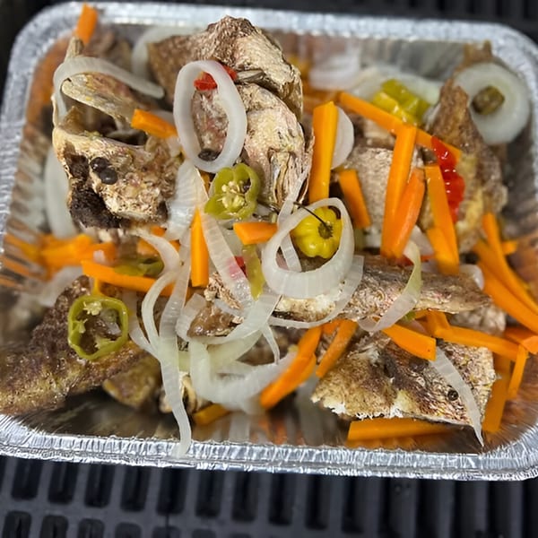 Jamaican escovitch fish with pickled onions, carrots, and peppers in a foil container.