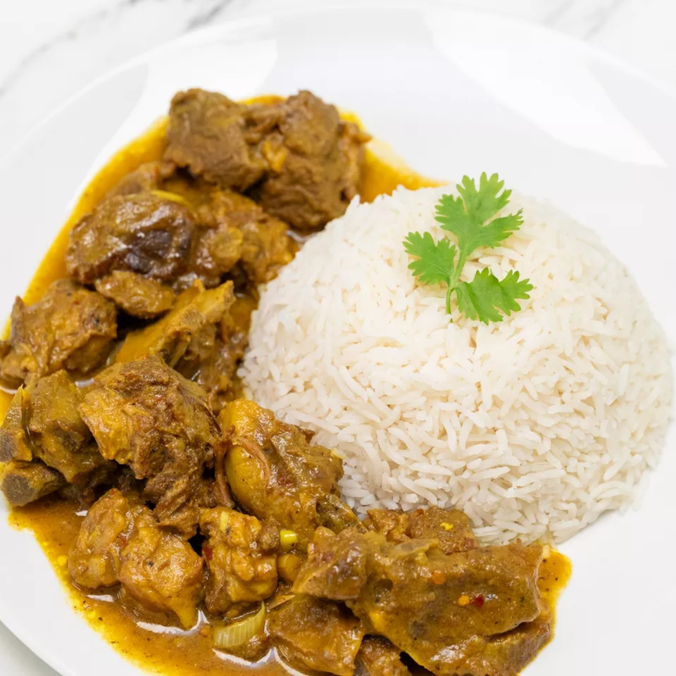 Plate of tender meat and vegetables in golden curry sauce served with white rice garnished with cilantro.