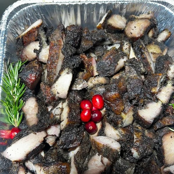 Close-up of 876 Jerk's jerk pork in a foil pan, garnished with rosemary and cranberries.