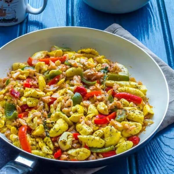 A white pan filled with Jamaican ackee and saltfish, red and green peppers, on a blue wooden table.