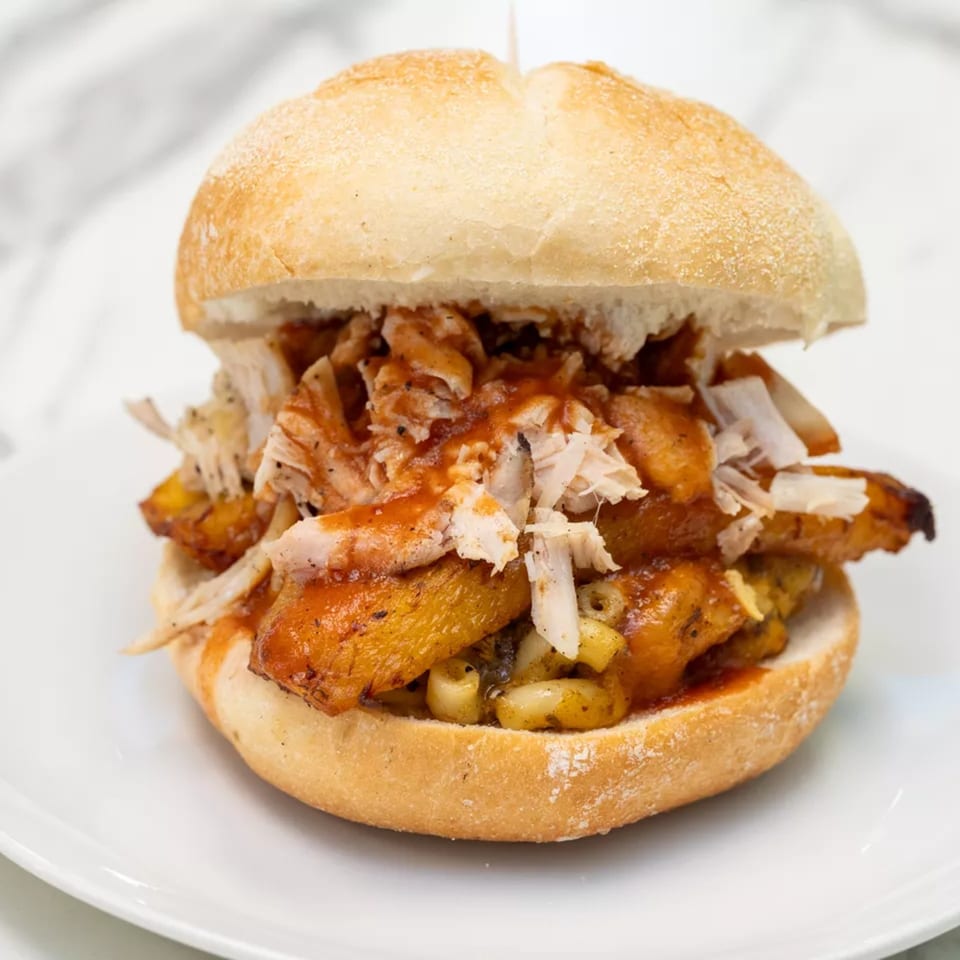 Crusty bread sandwich filled with roasted vegetables, shredded chicken, and sauce, served on a white plate.