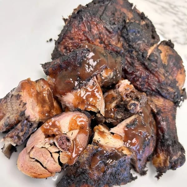 Close-up of 876 Jerk's Jamaican jerk chicken pieces, glistening with sauce on a white plate.