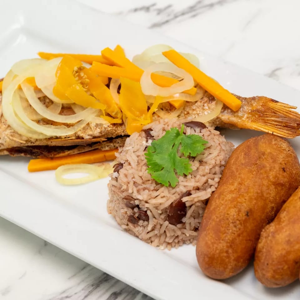 Plated grilled fish topped with onions and peppers, served with seasoned rice, fries, and golden fried croquettes.