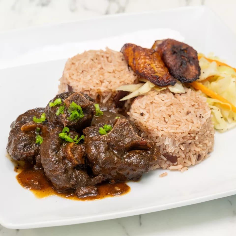 White plate of braised beef, seasoned rice, grilled sausages, and vegetables garnished with green onions.