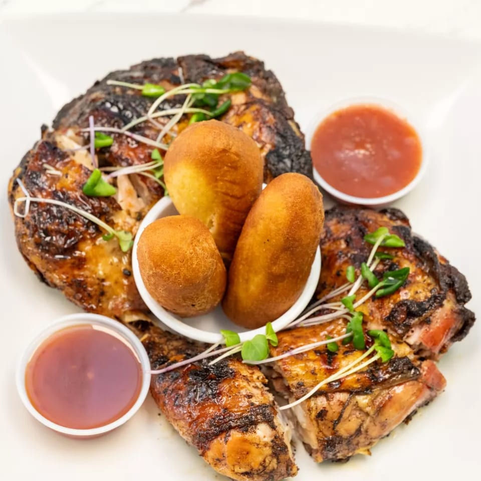 Grilled chicken pieces and golden croquettes garnished with microgreens, served with two bowls of reddish dipping sauce.