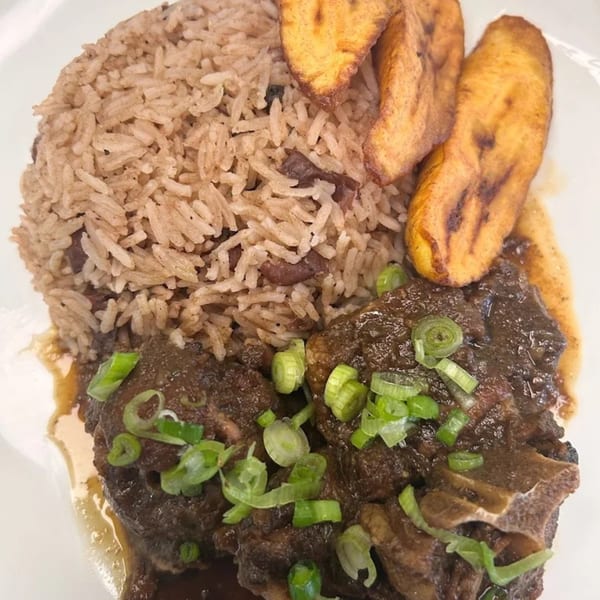 876 Jerk's Jamaican oxtail stew with rice and peas, garnished with green onions and fried plantains.