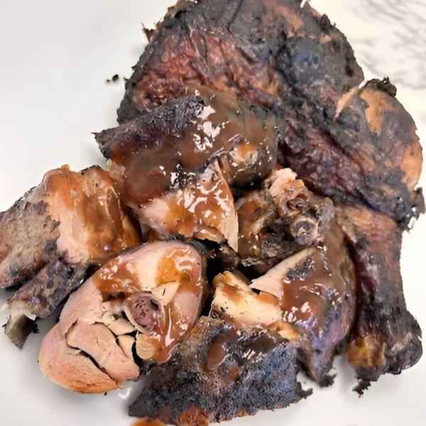 Close-up of 876 Jerk's Jamaican jerk chicken pieces with sauce on a white plate.