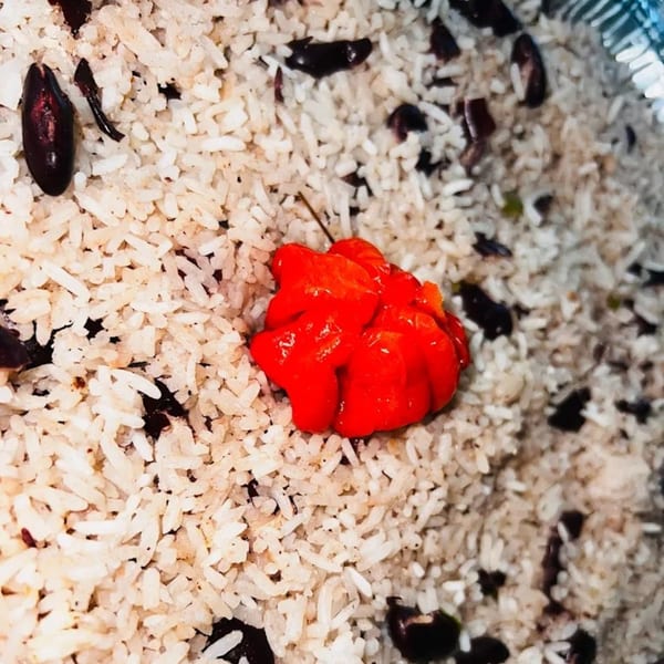 Close-up of Jamaican rice and peas with a vibrant red Scotch bonnet pepper on top.